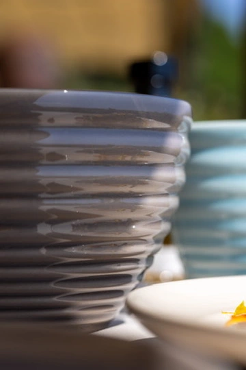 An extreme close-up of a glossy, étoupe-colored ceramic bowl by Kaya Ceramics, highlighting the handcrafted ribbed texture and grounded, honest weight.