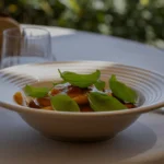 A close-up of a ribbed handmade ceramic pasta plate by Kaya Ceramics, filled with fresh pasta and basil on a sunlit outdoor table.