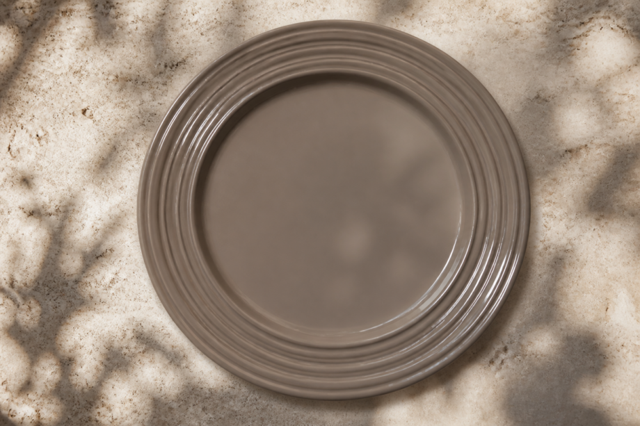 A handmade étoupe ceramic plate by Kaya Ceramics seen from above, its raised lines catching the afternoon light
